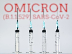 An illustration picture taken in London on December 2, 2021 shows four syringes and a screen displaying the word 'Omicron',  the name of the new covid 19 variant.