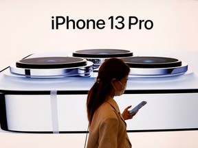 A woman wearing a face mask walks past an image of an iPhone 13 Pro at an Apple Store in Beijing, China, September 24, 2021.
