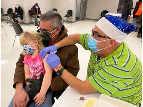 An Eastern Ontario Health Unit photo of Scott Halliday, right, giving Alexandra Page, 6, her first dose of COVID-19 vaccine, with her father Norman, on Dec. 1, 2021, in Alexandria, Ont.