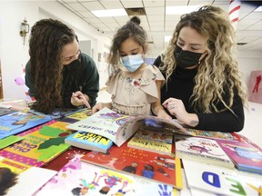 Beckie Berlasty, left, a researcher from St. Clair College, Payten Morencie, 8, and Danielle Couture-Atogwe from the Windsor Family Homes & Community Partnerships organization check out books at A Holiday Happening on Dec. 1, 2021.