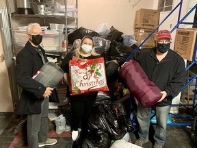 From left: Ed Hooft of the Windsor Curling Club seniors' association, Elizabeth Jewell of Street Help, and Jim MacLachlan of the Windsor Curling Club seniors' association hold up clothing and sleeping bag donations made by the association to Street Help on Dec. 6, 2021.