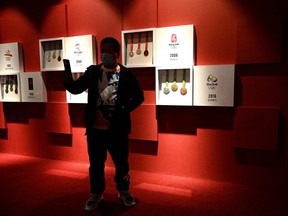 A man poses for a selfie in front of medals from past Olympic Games on display at the Beijing Capital Museum in Beijing on Jan. 6, 2022.