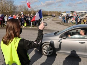 Supporters and members of the yellow vest movement hold French national flags in a parking lot of a shopping centre in Longueau as they cheer anti-COVID restrictions car drivers during their "Convoi de la liberte" (The Freedom Convoy), a vehicular convoy protest converging on Paris to protest COVID-19 vaccine and restrictions in France, Friday, Feb. 11, 2022.