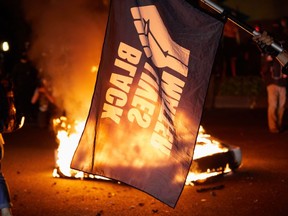 A Black Lives Matter flag waves in front of a fire at the North Precinct Police building in Portland, Oregon on September 6, 2020. - Protestors are marching for an end to racial inequality and police violence. Aaron Danielson, 39, a supporter of a far-right group called Patriot Prayer, was fatally shot August 29, 2020, in Portland, Oregon after he joined pro-Trump supporters who descended on the western US city, sparking confrontations with Black Lives Matter counter-protesters. (Photo by ALLISON DINNER/AFP via Getty Images)