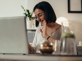 Femme utilisant un smartphone et un ordinateur portable pour une réunion en ligne avec ses collègues tout en travaillant à distance depuis chez elle
