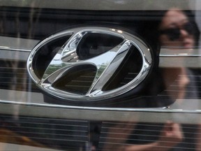 The company logo of Hyundai Motor on a Santa Fe sport utility vehicle and a woman's reflection is seen through the window of a Hyundai dealership in Seoul July 2, 2012.