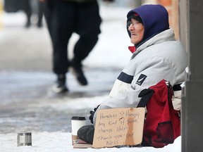 A homeless man sits on the sidewalk on Ouellette Avenue in downtown Windsor seeking spare change on Friday, Feb. 4, 2022.