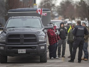 Demonstranten sprechen mit einem Polizeibeamten aus Windsor, der am Donnerstag, dem 10. Februar 2022, verhinderte, dass der Pick-up-Truck mit einem Anhänger in das blockierte Gebiet in der Wyandotte Street West einfuhr.