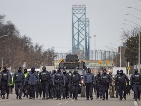 A large line of police officers march south on Huron Church Road on Saturday, Feb. 13, 2022, clearing protesters who have blockaded the road since Monday.