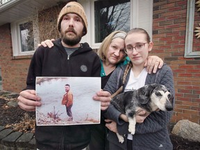 The family of Darrell Mills, 58, who was killed in an industrial accident on Monday, Michelle Tremblay-Mills, centre, wife, and children Darrell Jr. and Danielle pose with a photo of him at their LaSalle home on Wednesday, March 30, 2022. Included with the family is Danielle's dog Duke who she says her father jokingly referred to as his grandson.