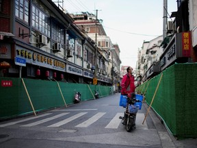 A delivery worker standing on a scooter looks over barriers in a closed residential area during lockdown, amid the coronavirus disease (COVID-19) pandemic, in Shanghai, China, May 9, 2022.