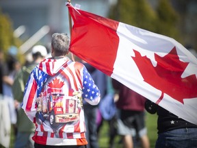 Ein Teilnehmer einer Anti-Lockdown-Kundgebung trägt am Samstag, den 7. Mai 2022, im Dieppe Park einen „Freedom Convoy“-Pullover, während er die kanadische Flagge trägt.