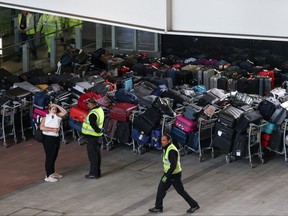 Airport workers stand next to lines of passenger luggage arranged outside Terminal 2 at Heathrow Airport in London, June 19, 2022.