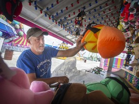Blair Haines sorts out the toy prizes for the Water Gun Fun game on Thursday, June 16, 2022, as workers set up for the start of the midway carnival at the Riverfront Festival Plaza after a two-year absence. The carnival runs until July 3.
