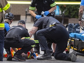 Windsor police and EMS paramedics treat a man suffering from a gun shot wound after he was shot by police while threatening people with a machete on Wyandotte Street West at Ouellette Avenue, on Monday, August 15, 2022.