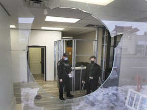 A Windsor officer and Alex Reid from W.E. Trans Support in Windsor, ON. are shown through a broken window on Monday, February 22, 2021 at the organization's office. It's the third vandalism event in a week at the group's location.
