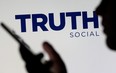 The Truth social network logo is seen displayed behind a woman holding a smartphone in this picture illustration taken Feb. 21, 2022.