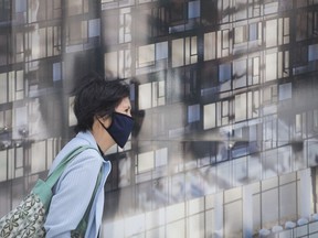 A woman wears a face mask as she walks by a photograph of an office building in Montreal, Saturday, Sept. 5, 2020.The mayor of a city west of Toronto says a six-week mask mandate has been established for municipal employees amid rising illness among staff and the community.THE CANADIAN PRESS/Graham Hughes