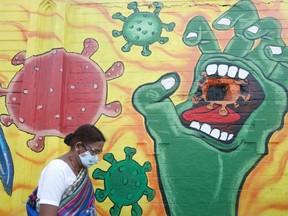 A woman wearing a protective face mask walks past a mural on a street, amidst the spread of COVID-19, in Mumbai