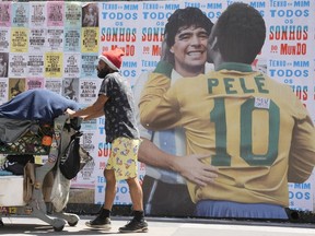 A man pushes a cart loaded with garbage for recycling in front of a mural depicting Brazilian soccer legend Pele embracing late Argentinean soccer star Diego Maradona in Sao Paulo, Brazil, Saturday, Dec. 24, 2022. Pele is hospitalized to continue his cancer treatment.