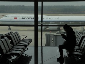 A passenger checks her phone as an Air China passenger jet taxi past at the Beijing Capital International airport in Beijing, Oct. 29, 2022. China will drop a COVID-19 quarantine requirement for passengers arriving from abroad starting Jan. 8. The National Health Commission announced the change Monday, Dec. 26, 2022 as part of the latest easing of China's once strict virus control measures.