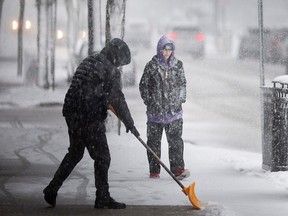 A shop owner shovels the sidewalk on Ottawa Street while a pedestrian walks past during a significant snow storm on Wednesday, Jan. 25, 2023.