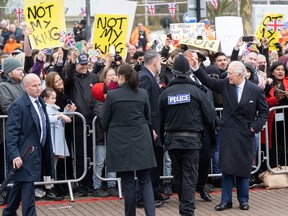 Demonstrators hold signs reading "Not My King" as Britain's King Charles III (right) waves at well-wishers upon arriving at the Church of Christ the Cornerstone in Milton Keynes, north of London, Thursday, Feb. 16, 2023.
