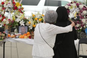 Xan Hoang (right) is comforted by a supporter during a memorial service for two men, including her husband Ban Phuc Hoang, in Edmonton's Chinatown, on Friday May 19, 2023. Hoang and Hung Trang were killed in separate attacks in the area on May 18, 2022.