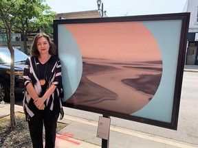 Art Windsor Essex executive director Jennifer Matotek stands next to a reproduction of a painting by Canadian artist Wanda Koop, posted on Ottawa Street in Windsor as part of the AWE's Look Again! Outside campaign. Photographed June 2, 2023.