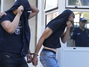 Soccer fans covering their faces, most of them from Croatia, are escorted by police as they leave the Athens Police Headquarters, Greece, Wednesday, Aug. 9, 2023. Ninety-four fans of Croatia's Dinamo Zagreb are appearing in court this morning for a preliminary hearing over Monday night's fan violence that left a fan of Greece's AEK dead and another eight people injured.