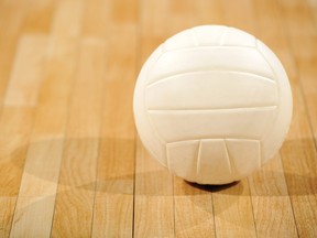 A lone white volleyball sitting on a wooden floor