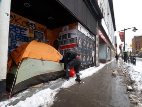 A man attaches a lock to the zip up door on the tent he has set up in front of the doors of a closed business on Bank Street in Ottawa.