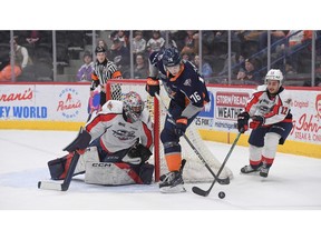 Windsor Spitfires' goalie Joey Costanzo keeps an eye on Flint Firebirds' forward Nathan Aspinall (76) while Windsor teammate Ryan Abraham (12) battles for the puck during Friday's game at the Dort Financial Center in Flint.