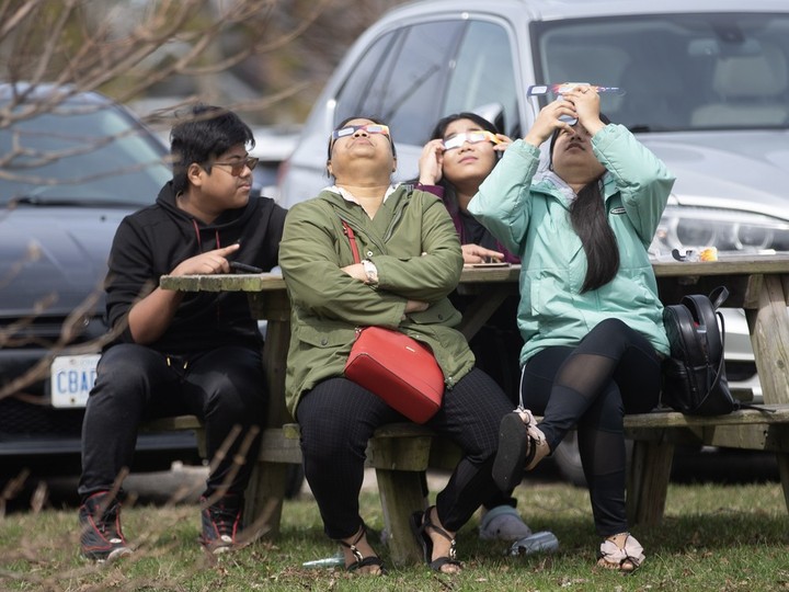  Dawslom Peter (centre left) sits with family, dons special glasses, and looks at the sun as it is eclipsed by the moon at Mettawas Park in Kingsville on Monday, April 8, 2024.