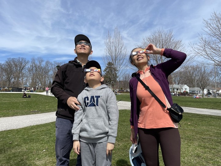  David Wang, Isiah Wang and Judy Chang look up at the partial eclipse with safety sun glasses at Seacliff Park Monday, April 8, 2024.