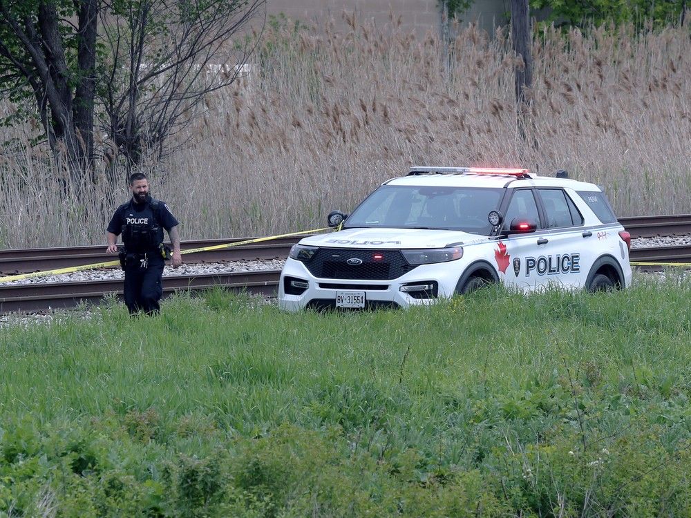 Several police units and a forensic unit is on the scene beside the railroad tracks