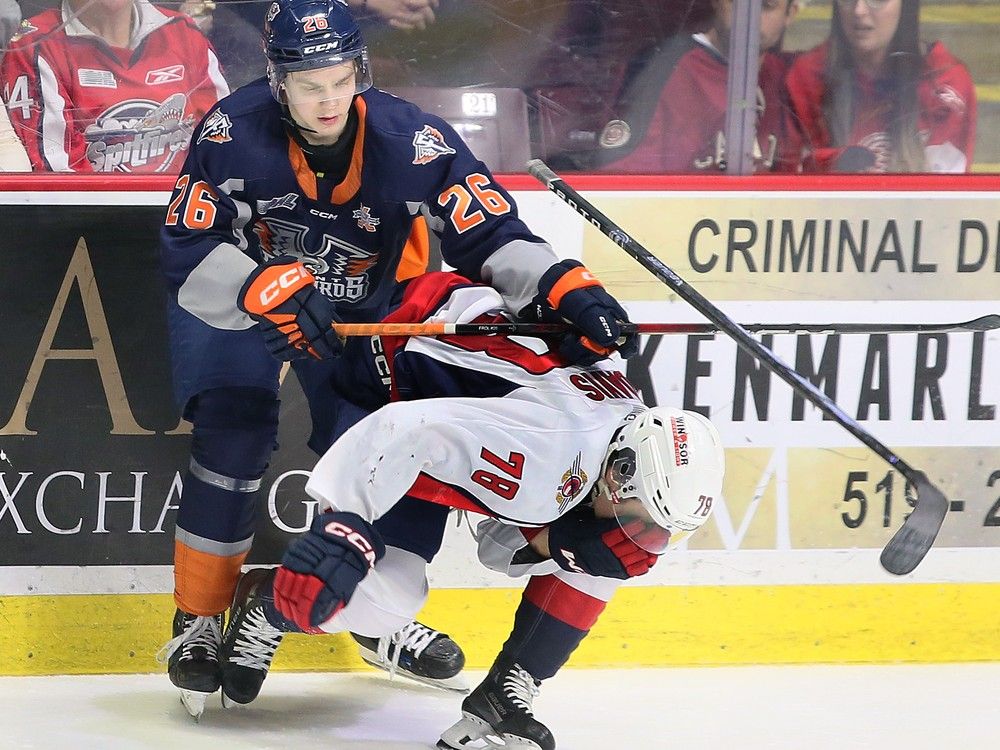 El defensa de los Windsor Spitfires, Tanner Winegard, izquierda, lucha con el delantero de los Flint Firebirds, Matthew Wang, frente al portero de los Windsor, Joey Costanzo, durante el partido del martes en el Centro WFCU.