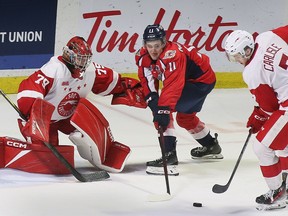 Windsor Spitfires's supersuper forward Noah Morneau center hunts down a rebound in front of Sault Ste. Marie Greyhounds goalkeeper Nolan Lalonde and defensive Caeden Carlisle Saturday.