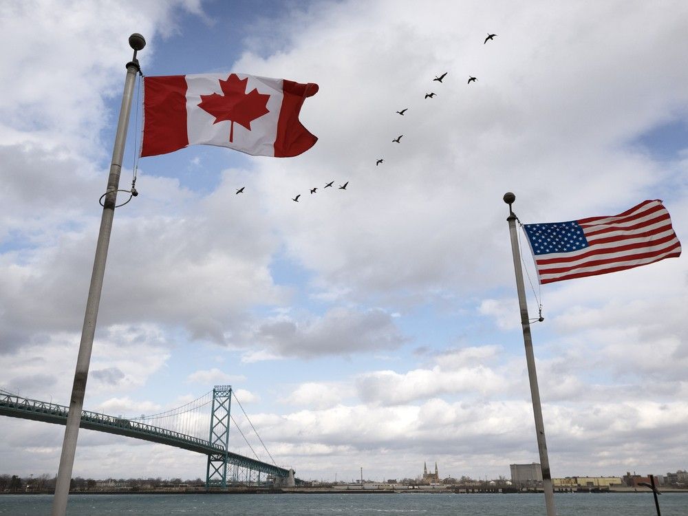 A Canadian and American flag fly along the Detroit River in Windsor on Friday, Feb. 20, 2026, with the Ambassador Bridge in the background.