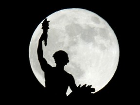 The Golden Boy stands in silhouette against a full (looking) moon.n/a