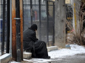 A homeless man sits on a concrete barrier.