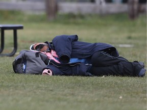 A person sleeps under a heavy coat, in a park adjacent to a parking lot, in Winnipeg. Tuesday.