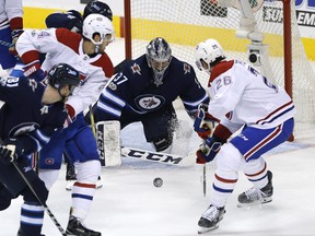 Jets goaltender Connor Hellebuyck tries to stop Montreal’s Phillip Danault (centre left) and Jeff Petry as they storm the net.