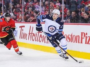 Nikolaj Ehlers (27) of the Winnipeg Jets carries the puck against Matt Stajan (18) of the Calgary Flames, Saturday night in Calgary.
