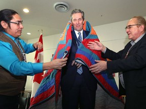 Premier Brian Pallister (centre) is presented a gift by Sapotaweyak Cree Nation Chief Nelson Genaille (left) and Fisher River Cree Nation Chief David Crate following an announcement of funding for high-speed internet in rural and remote Manitoba communities at the Millennium Library in Winnipeg on Tuesday.