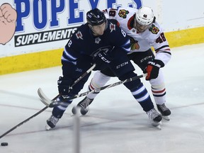 Winnipeg Jets defenceman Jacob Trouba (left) is pressured by Chicago Blackhawks forward Vinnie Hinostroza in Winnipeg Thursday. (Kevin King/Winnipeg Sun)