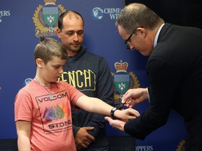 Gavin Demers, who has autism, is presented with a MedicAlert bracelet by MedicAlert president/CEO Robert Ridge as his father Pierre watches during a press conference at Winnipeg Police Service headquarters on Smith Street in Winnipeg on Thurs., March 1, 2018. Kevin King/Winnipeg Sun/Postmedia Network