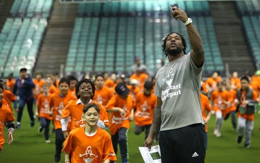 Saskatchewan Roughriders running back Jerome Messam  uses his phone to capture students running a lap during a Jumpstart event at the RBC Convention Centre that is part of CFL Week in Winnipeg on Thurs., March 22, 2018. Over 150 kids from Greenway and Victory schools were able to participate in drills with current CFL stars. Kevin King/Winnipeg Sun/Postmedia Network