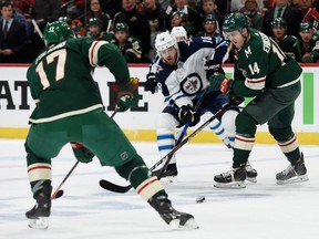 Joel Eriksson Ek (14) of the Minnesota Wild gets the puck away from Bryan Little (18) of the Winnipeg Jets as teammate Marcus Foligno (17) looks on during the first period in Game 3 Sunday.