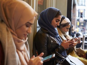 In this stock photo, a group of young Muslim women use their cellphones wearing hijabs.